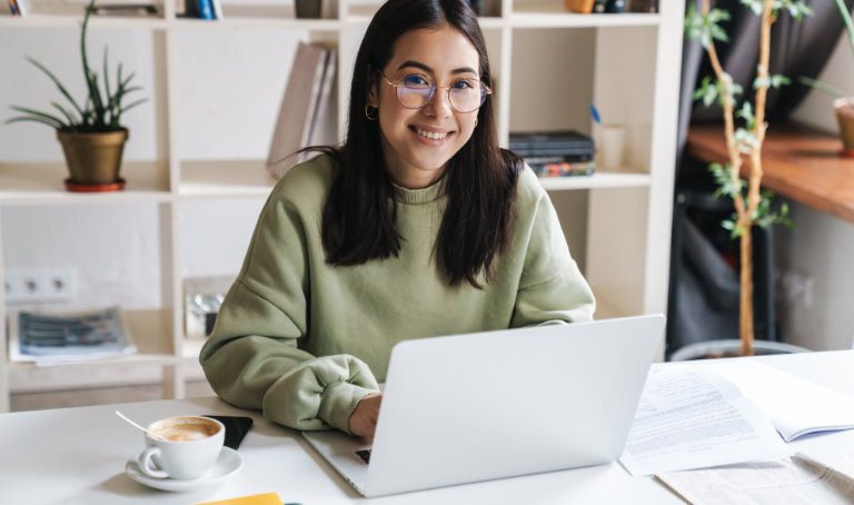 A woman sitting down in front of her laptop smiling at the camera