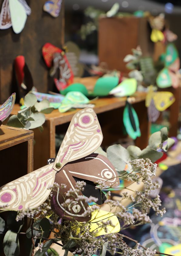 A wooden shelf sits on a colourful table covered with decorated paper moths 