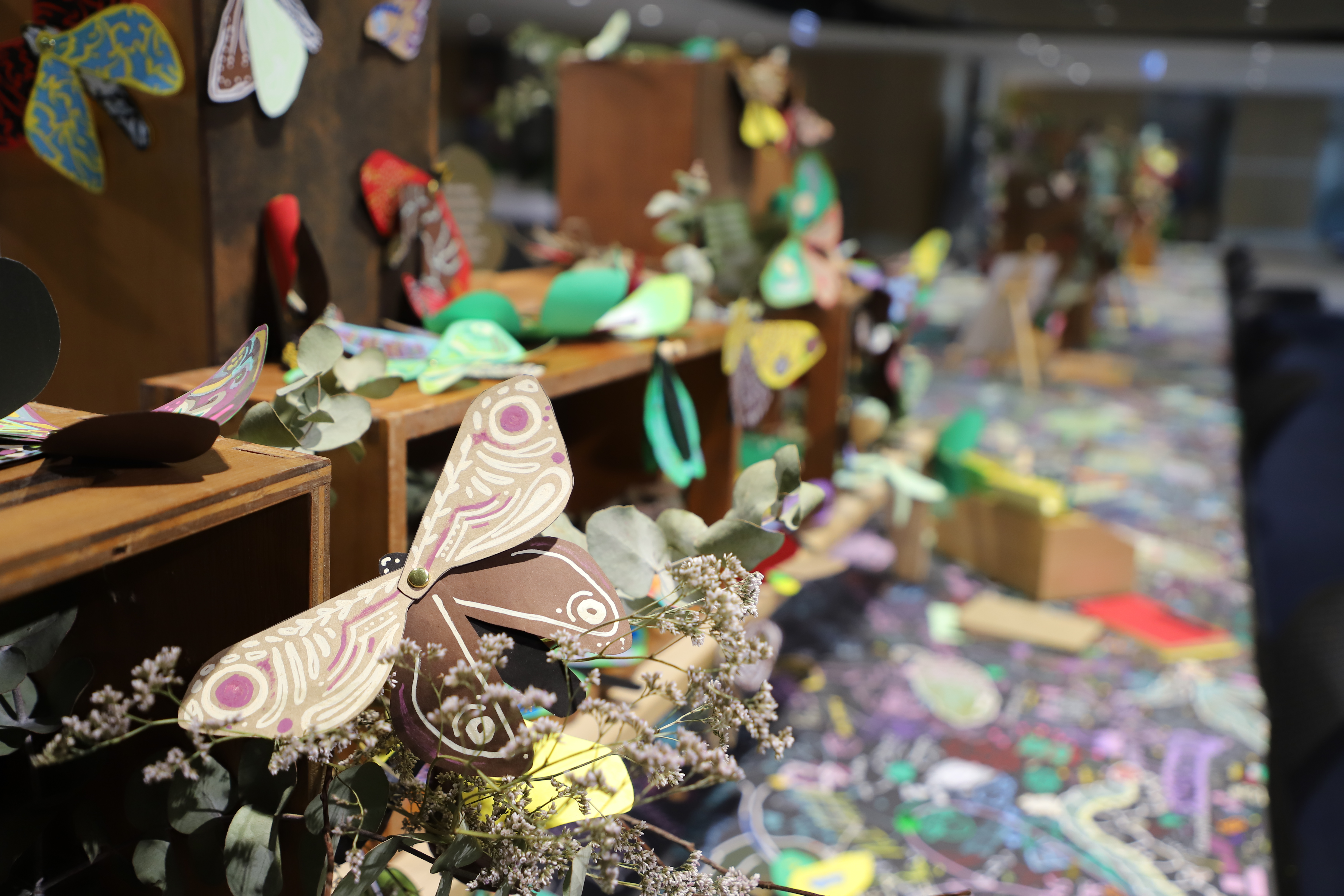 A wooden shelf sits on a colourful table covered with decorated paper moths 