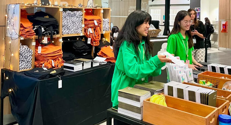 Students in green hoodies giving out free orange and black tote bags