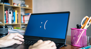 Computer with black background with a white sad face on the screen