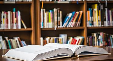 Open book on table in front of bookshelves