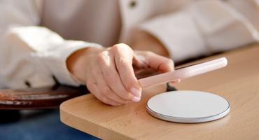 A hand holds a pink mobile over a white circular wireless charging device