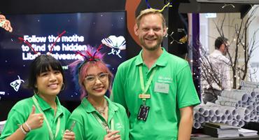 Student staff in green shirts grinning and smiling at camera