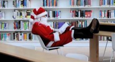 Santa sits in the Library with his feet up on a desk, reading a book