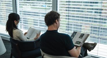 Two researchers sit side-by-side in armchairs with back facing us, reading 