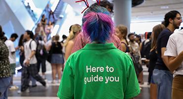 Student Guide standing with back to camera facing a crowd of people mingling
