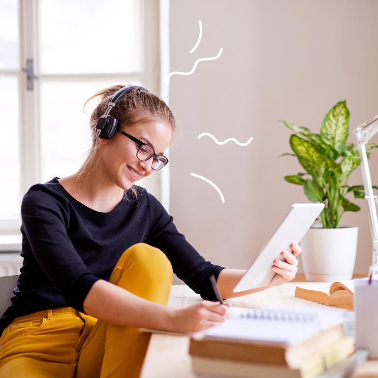 Woman with headphones at desk looking happily at tablet