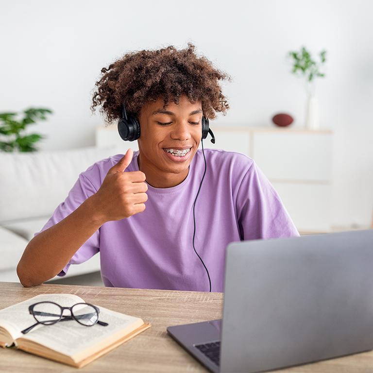 Man in purple shirt giving thumbs up to his laptop—he's winning at studying