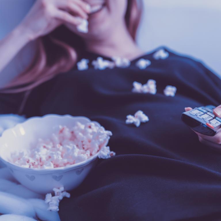 Woman reclining with popcorn and TV remote.