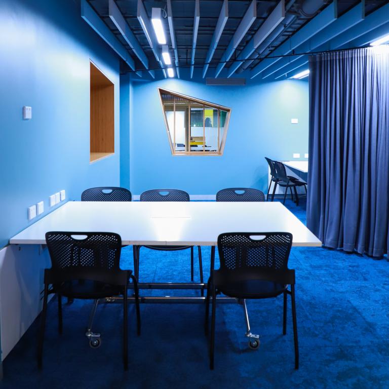 A room with blue walls, a table and chairs, blue curtains and internal windows that are polygons.