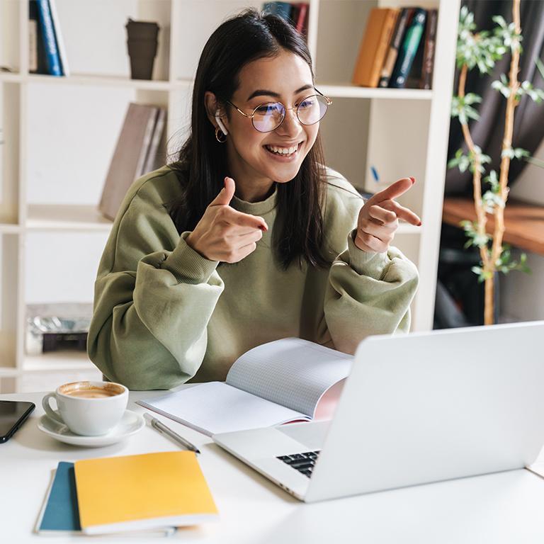 Woman smiling and pointing finger guns at a laptop.