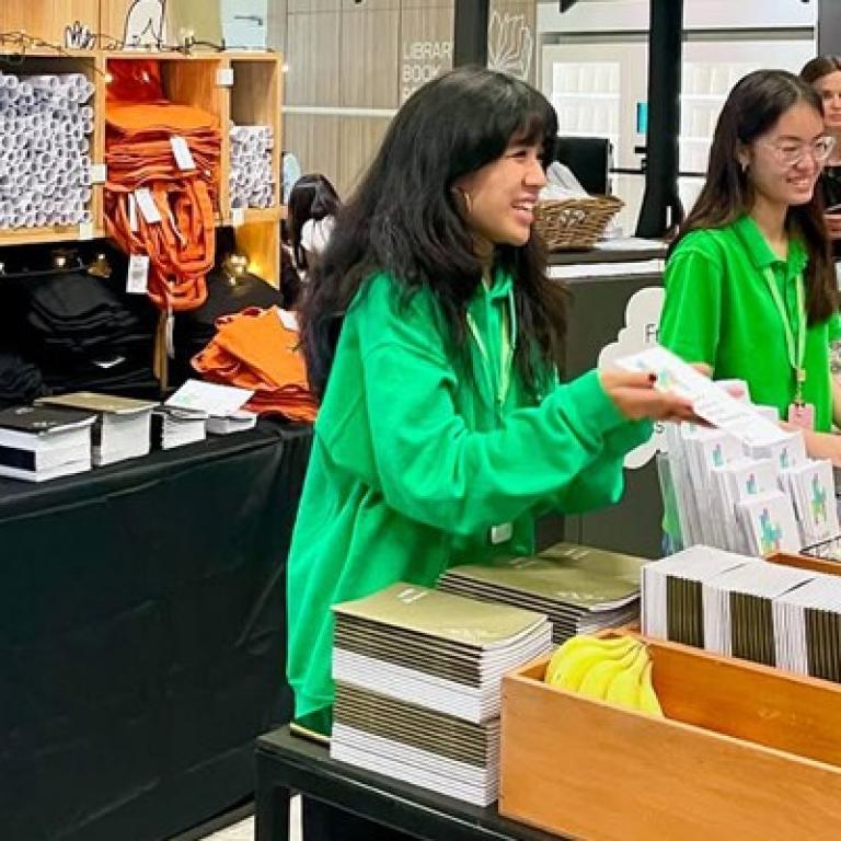 People in green hoodies handing out free brochures and tote bags