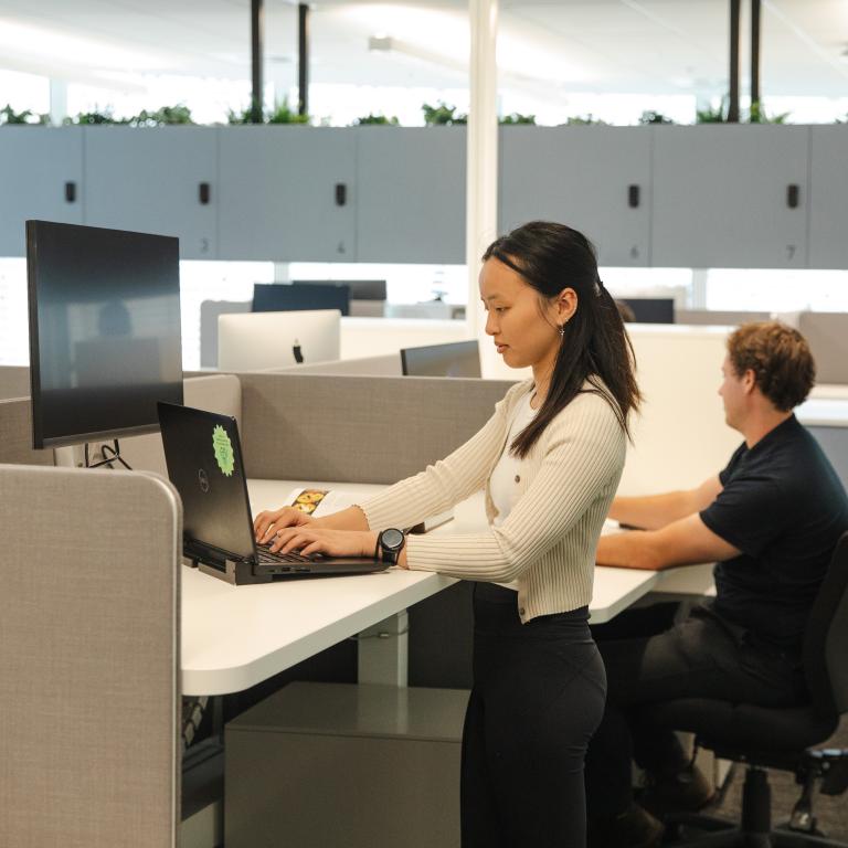 Woman standing at desk typing on a laptop