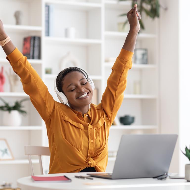 Student in yellow sweater raising arms in joy at laptop