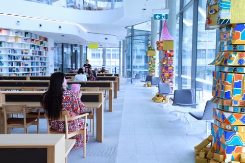 Creative in Residence Raquel Caballero sitting at a wooden desk, gazing to the right at her large papier mache sculptures