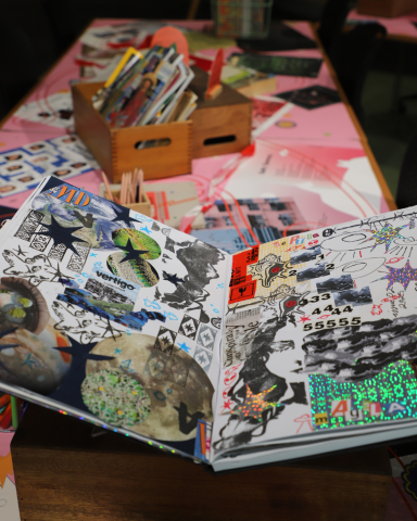 Large community scrapbook open to 2 collaged pages sitting on a pink table