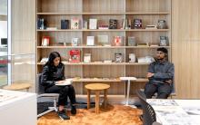 A man and woman sitting down reading in front of a wooden book case