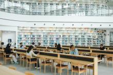 Students studying at wooden desks inside a library with floor to ceiling bookcases